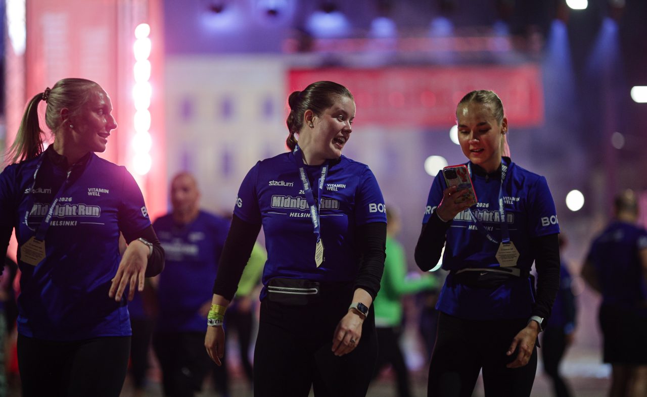 Tre tjejer som kommit i mål med medalj runt halsen som kollar sitt resultat i mobilen efter Midnight Run Helsinki 2026