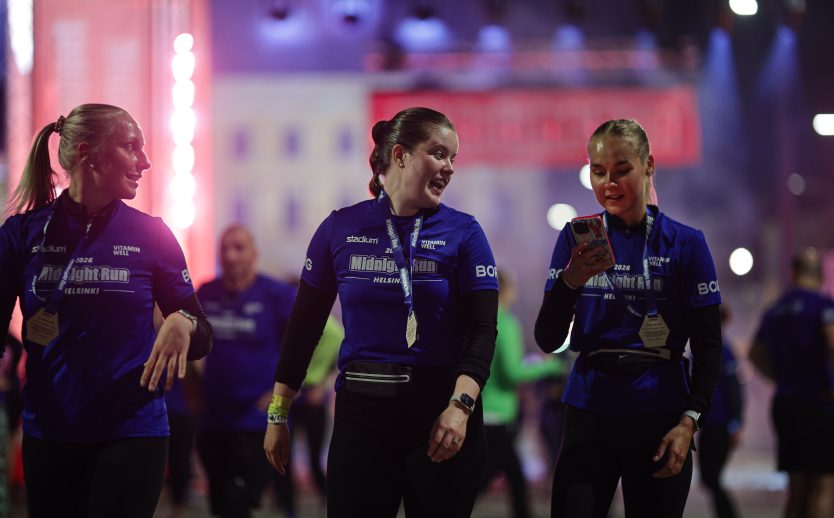 Tre tjejer som kommit i mål med medalj runt halsen som kollar sitt resultat i mobilen efter Midnight Run Helsinki 2026
