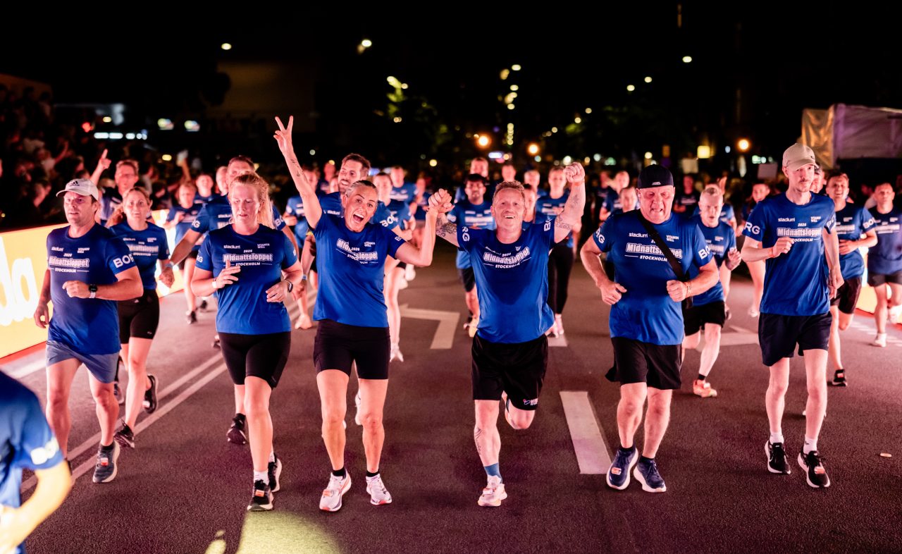 Löpare håller hand i hand på vägen in mot mål under Midnattsloppet Stockholm 2026