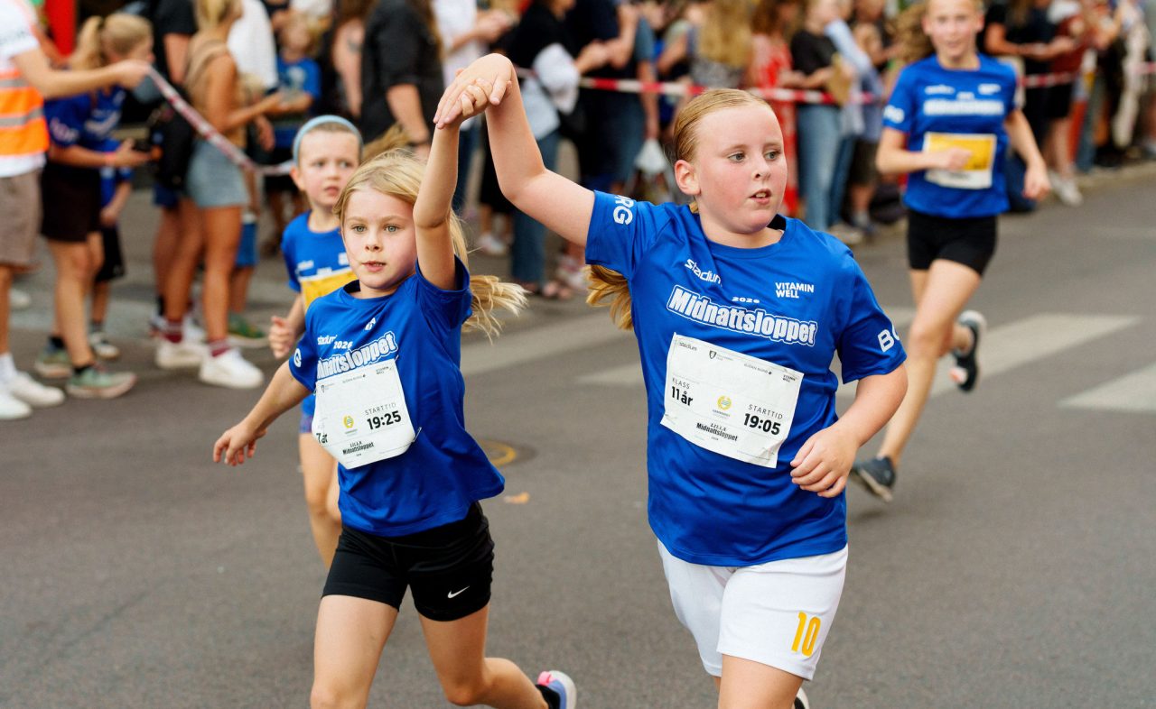 Två tjejer som springer hand i hand mot målet under Lilla Midnattsloppet 2026