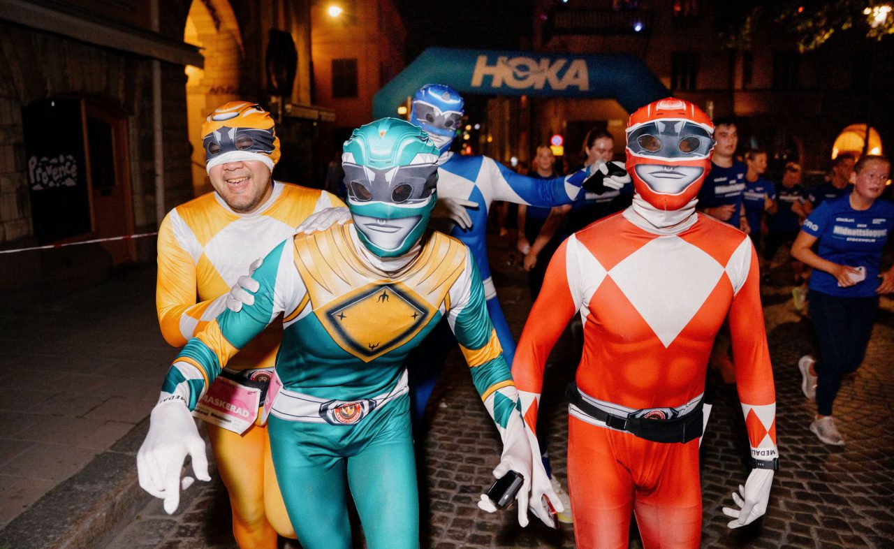 Maskeraddeltagare utklädda till superhjältar springer förbi HOKAs banaktiviteter under Midnattsloppet Stockholm 2026