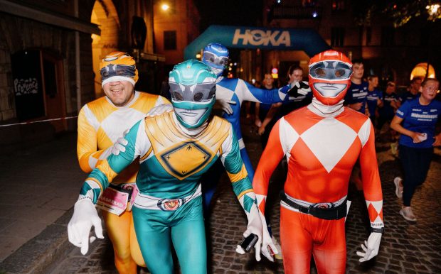 Maskeraddeltagare utklädda till superhjältar springer förbi HOKAs banaktiviteter under Midnattsloppet Stockholm 2026